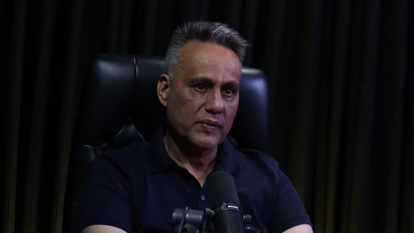 Rogério Furtado com expressão séria durante entrevista ao podcast Encampus, sentado em cadeira de couro preta
