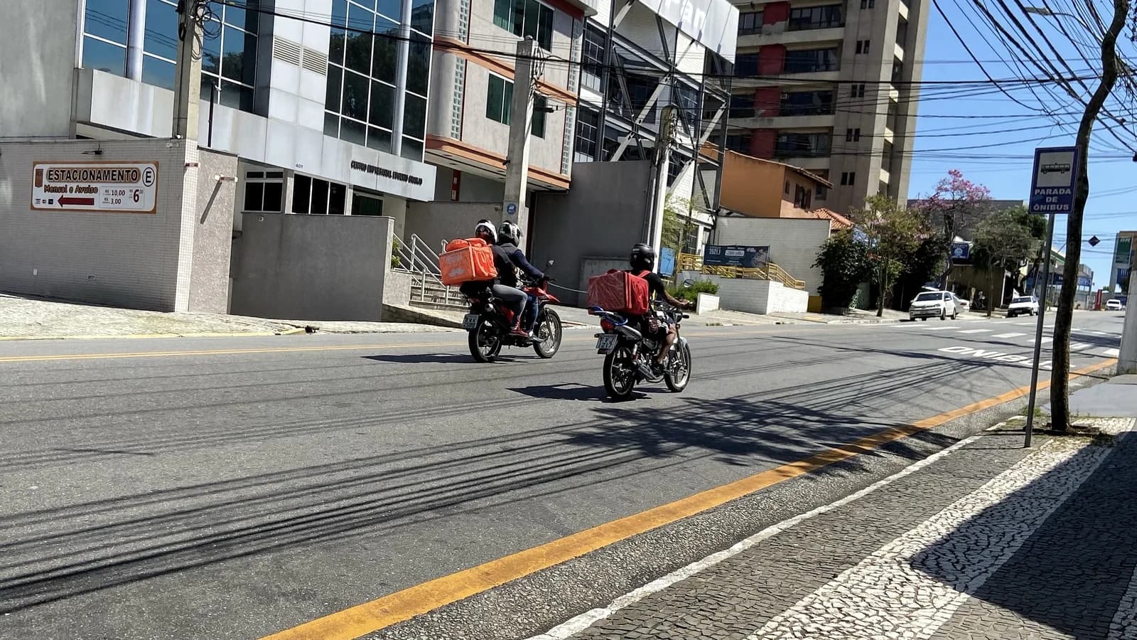 Entregadores de motocicleta circulam por via urbana no Brasil fazendo coleta e entrega de encomendas