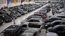 Vista aérea de um pátio de loja de veículos usados, com carros enfileirados e um funcionário caminhando entre eles