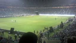 Interior da Arena do Grêmio lotada durante uma partida, com o gramado iluminado