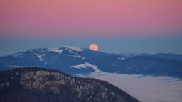 Lua cheia alaranjada surgindo no horizonte ao entardecer, atrás de uma montanha