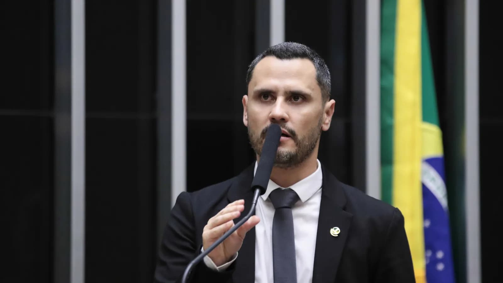 O senador Cleitinho discursa ao microfone na tribuna, com a bandeira do Brasil ao fundo