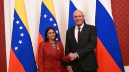 Delcy Rodríguez, presidente interina da Venezuela, cumprimenta autoridade em evento oficial, com bandeiras da Venezuela e da Rússia ao fundo
