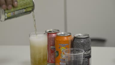 Pessoa serve refrigerante em copo, com outras latas ao fundo, ilustrando consumo de alimentos ultraprocessados