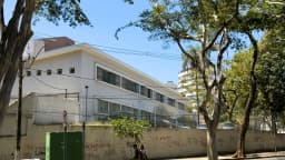 Fachada de escola da rede estadual em Belo Horizonte, com estudantes passando na calçada