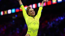 Rebeca Andrade comemora com os braços erguidos, uniforme amarelo do Brasil