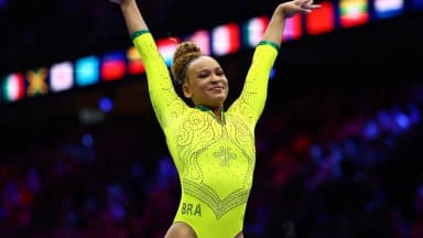 Rebeca Andrade comemora com os braços erguidos, uniforme amarelo do Brasil
