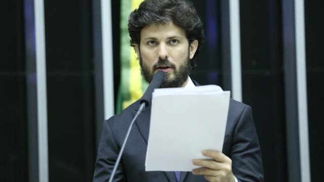 Marcelo Aro fala ao microfone em audiência pública, de terno escuro e barba