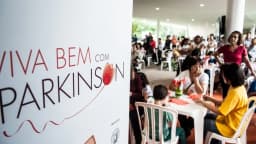 Banner da campanha Viva Bem com Parkinson ao lado de pessoas reunidas em evento de conscientização sobre a doença