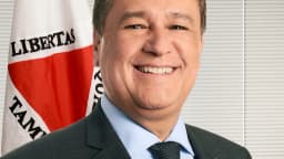 O senador Carlos Viana (PSD-MG) sorrindo, em retrato oficial, com a bandeira de Minas Gerais ao fundo