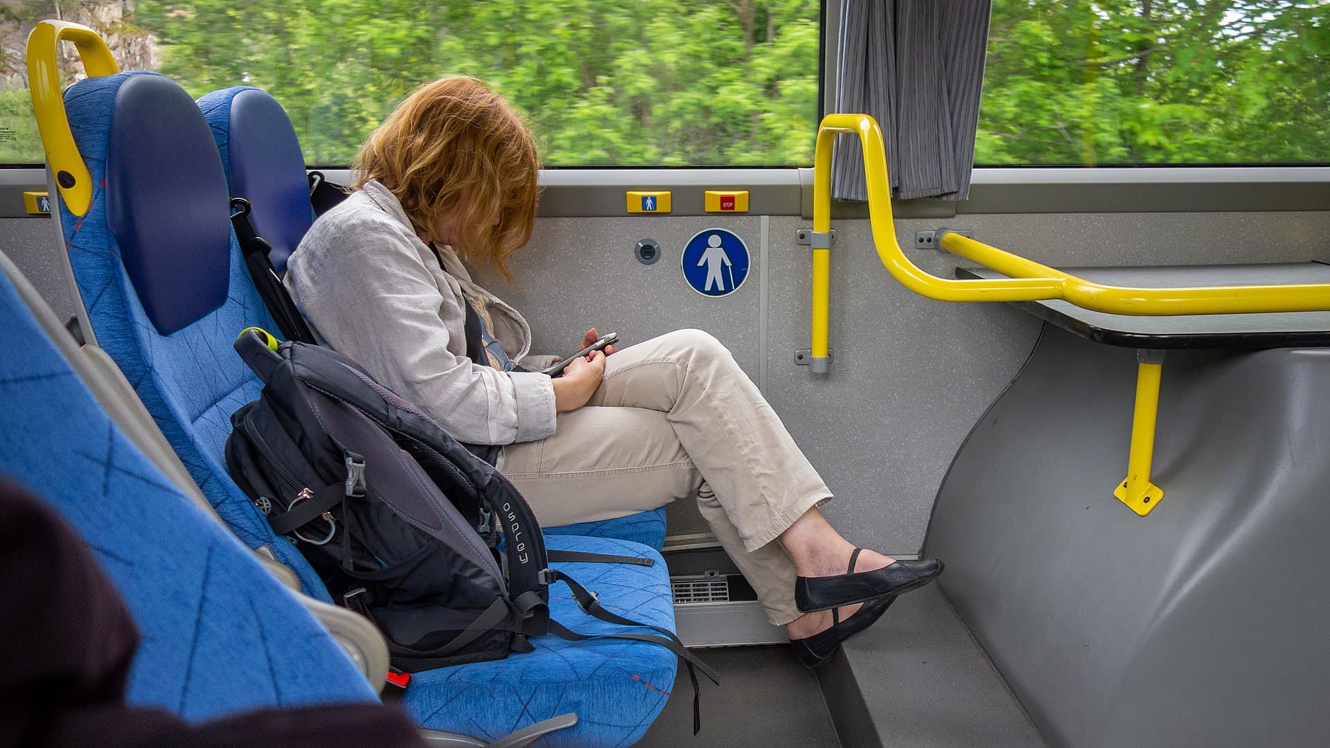 Passageira sentada em ônibus em movimento olha para a tela do celular, com a paisagem desfocada pela janela
