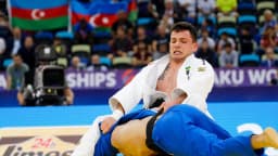 Judoca brasileiro, de judogi branco com a bandeira do Brasil, disputa luta contra adversário de judogi azul em campeonato mundial