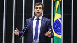 O deputado federal Nikolas Ferreira discursa na tribuna da Câmara dos Deputados, ao microfone e gesticulando, com a bandeira do Brasil ao fundo. Imagem de arquivo de fevereiro de 2023.