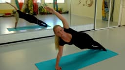 Mulher pratica exercício de pilates em prancha lateral sobre colchonete em estúdio