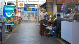 Pessoas sentadas comendo em mesas de uma cafeteria de mercado municipal