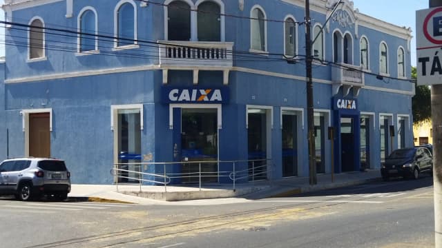 Fachada de agência da Caixa Econômica Federal em prédio histórico azul, com logo da Caixa na entrada