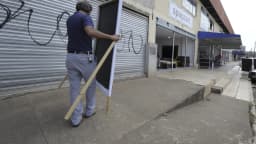 Homem instala placa de propaganda eleitoral em calçada de rua comercial