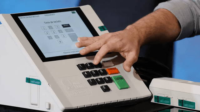 Mão testa o teclado de uma urna eletrônica durante demonstração do TRE para as Eleições 2026