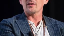 Ethan Hawke em close durante entrevista, com colar e blazer listrado