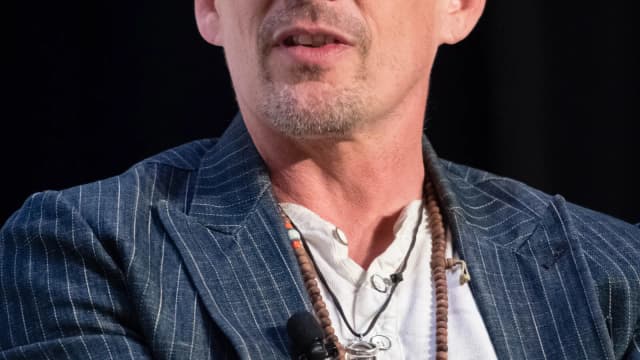 Ethan Hawke em close durante entrevista, com colar e blazer listrado