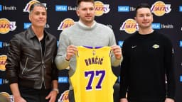 Luka Doncic segura a camisa 77 dos Lakers ao lado de dirigentes da equipe