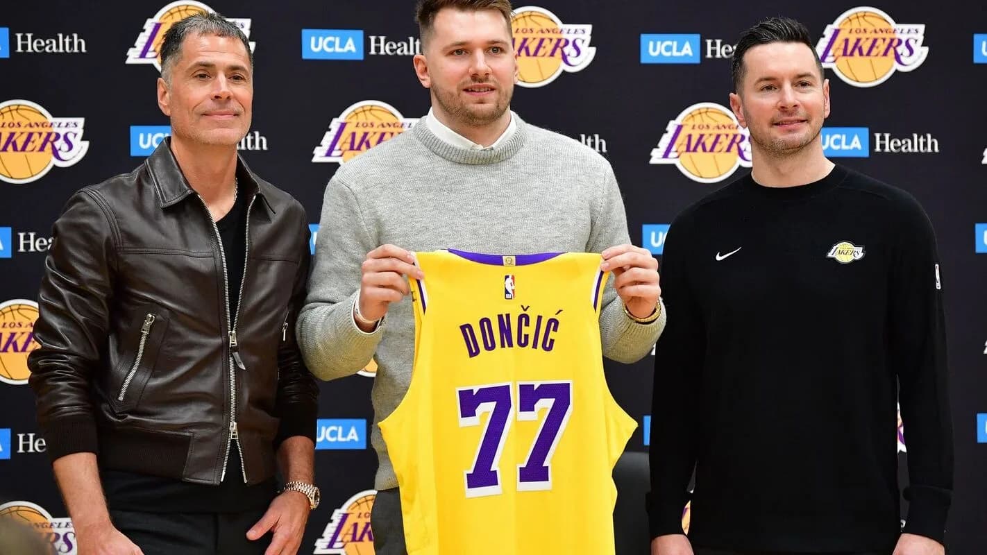 Luka Doncic segura a camisa 77 dos Lakers ao lado de dirigentes da equipe
