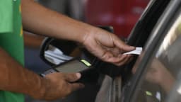 Mão de atendente de posto de combustível segura bico de abastecimento próximo a veículo