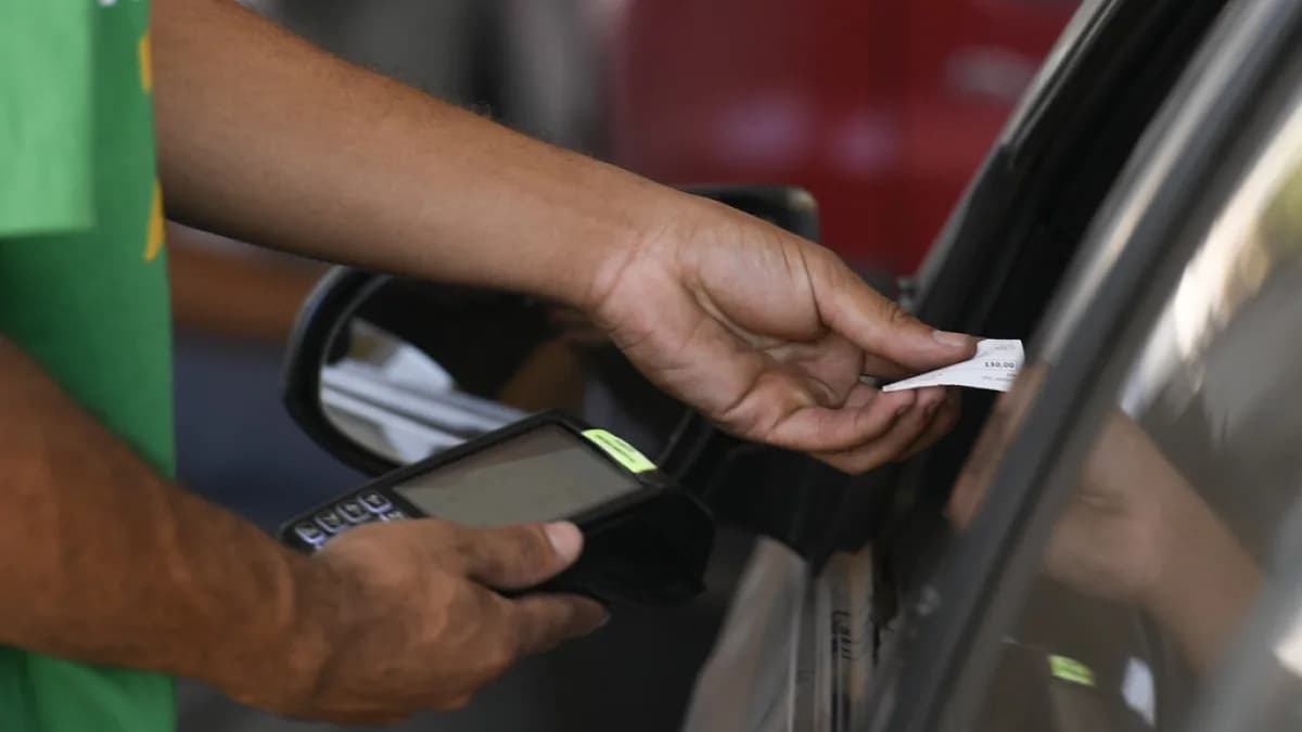 Mão de atendente de posto de combustível segura bico de abastecimento próximo a veículo