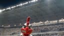 Mascote Galo Doido em primeiro plano com a Arena MRV lotada e iluminada ao fundo