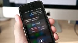 Pessoa segura iPhone exibindo a tela da Siri com um lembrete criado por voz