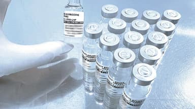 Mão com luva segura frasco de vacina contra Covid-19 de RNA mensageiro ao lado de outros frascos do estudo de estabilidade da Fiocruz