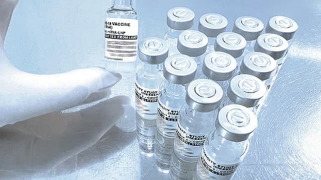 Mão com luva segura frasco de vacina contra Covid-19 de RNA mensageiro ao lado de outros frascos do estudo de estabilidade da Fiocruz