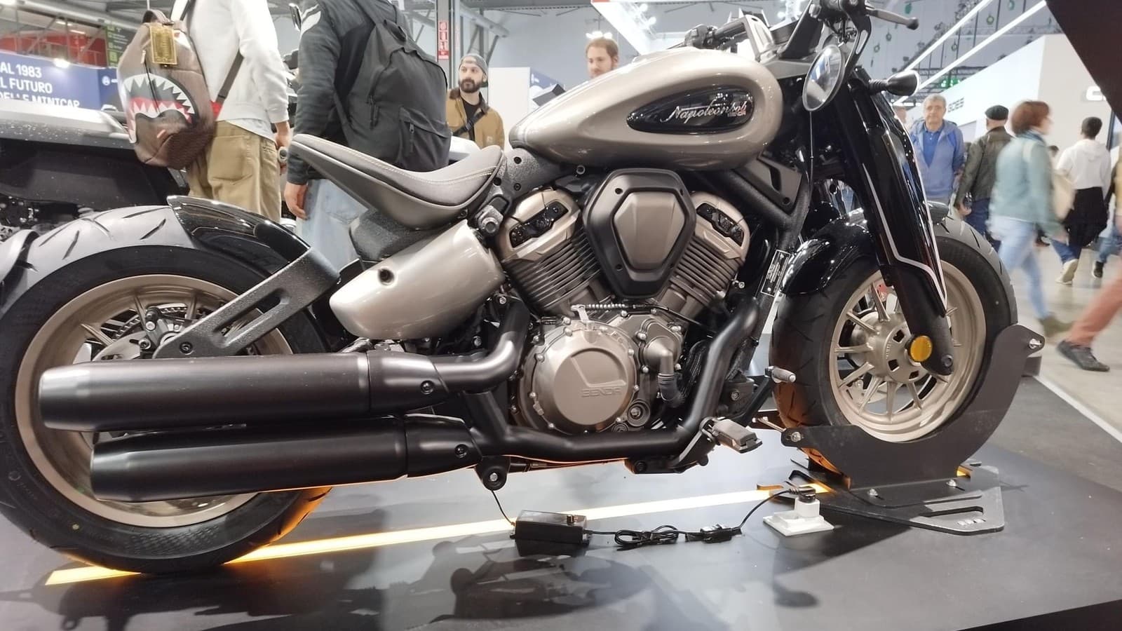 Moto custom Benda Napoleonbob exposta sobre plataforma em salão de motocicletas, com visitantes circulando ao fundo