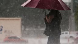 Pessoa com guarda-chuva vermelho protege-se de chuva forte em via urbana