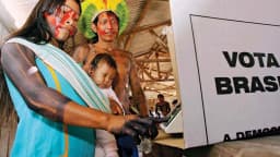 Indígena do Vale do Javari vota em urna eletrônica com cartaz 'Vota Brasil' ao fundo