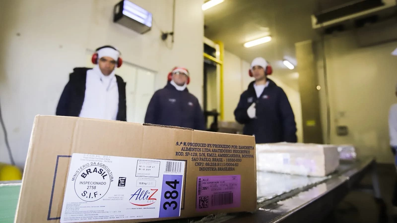 Caixa de exportação de frango com selo de inspeção do Ministério da Agricultura em frigorífico brasileiro, com trabalhadores ao fundo