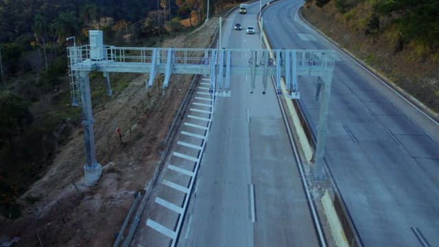 Vista aérea de trecho da rodovia BR-381 com pórtico de pedágio eletrônico, sem veículos no momento do registro