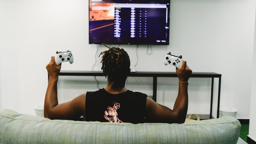 Jogador segura dois controles de videogame em frente à TV, foto ilustrativa