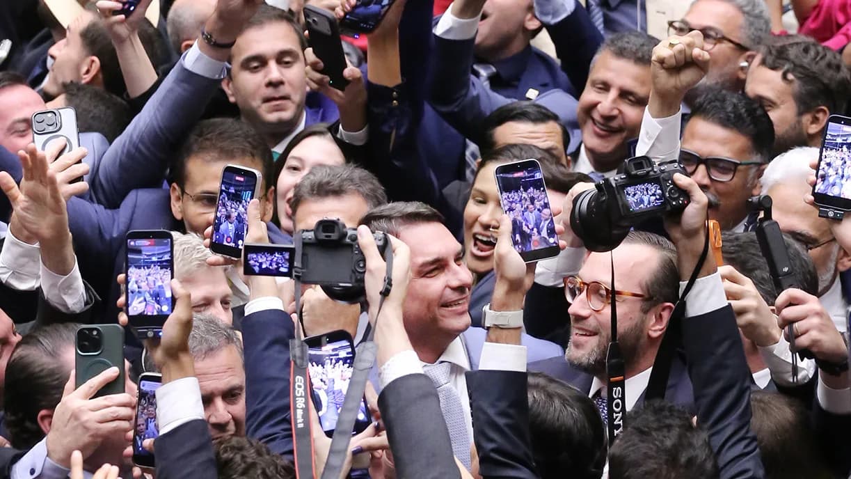 Flávio Bolsonaro sorri em meio a parlamentares que comemoram na Câmara dos Deputados, em abril de 2026