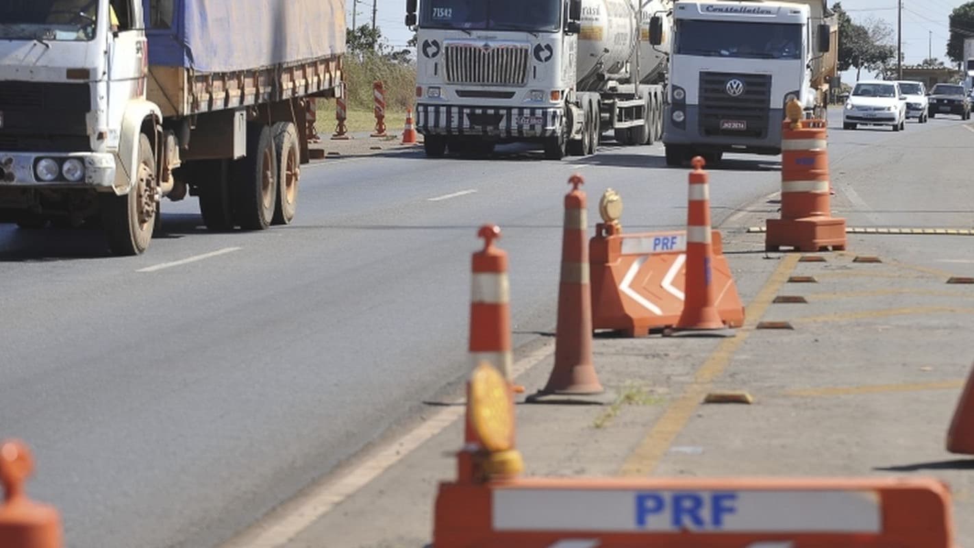 Rodovia federal com fluxo de caminhões e sinalização da Polícia Rodoviária Federal no acostamento, foto de arquivo