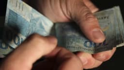 Mão conta cédulas de dinheiro do Banco Central do Brasil