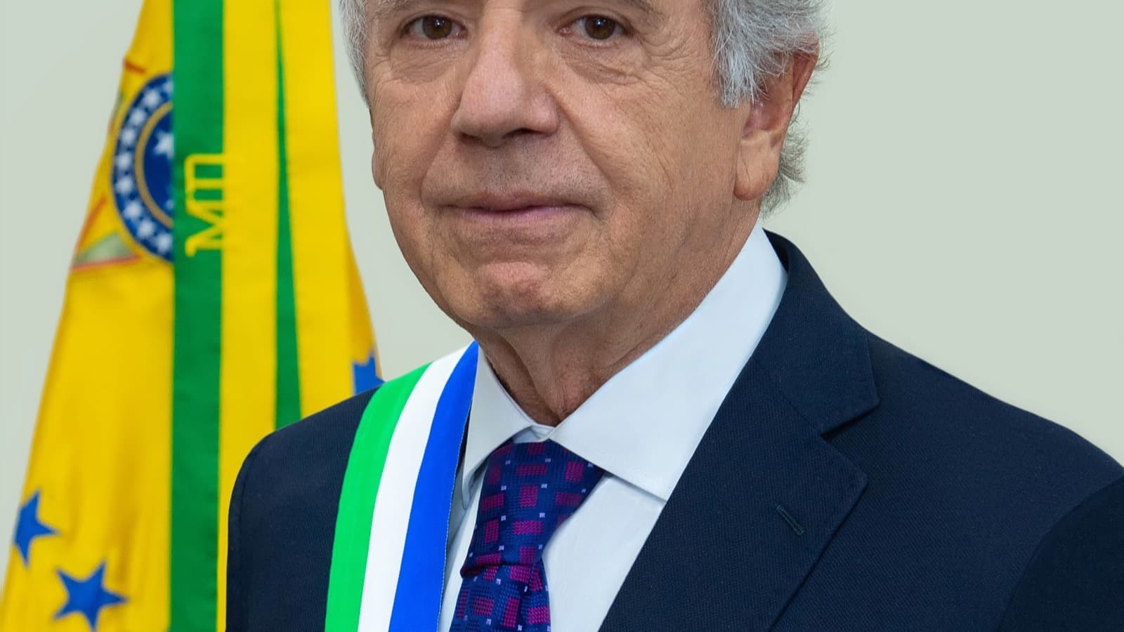 Retrato oficial do ministro da Defesa José Múcio, com faixa e bandeira do ministério ao fundo