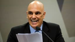 Ministro Alexandre de Moraes durante sabatina, de terno escuro, segurando papéis e falando ao microfone