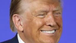 Donald Trump sorri durante evento público, vestindo terno escuro e gravata azul