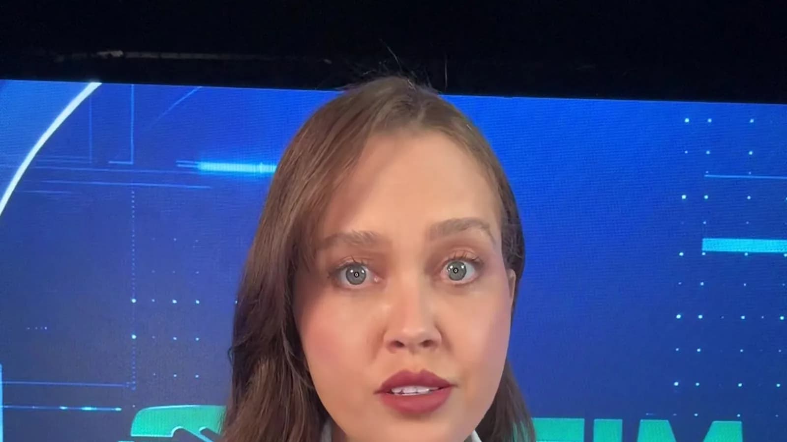 Repórter da TV Sim Brasil, de camisa clara e crachá de imprensa, fala direto para a câmera em frente ao letreiro do estúdio para explicar o fim da taxa das blusinhas