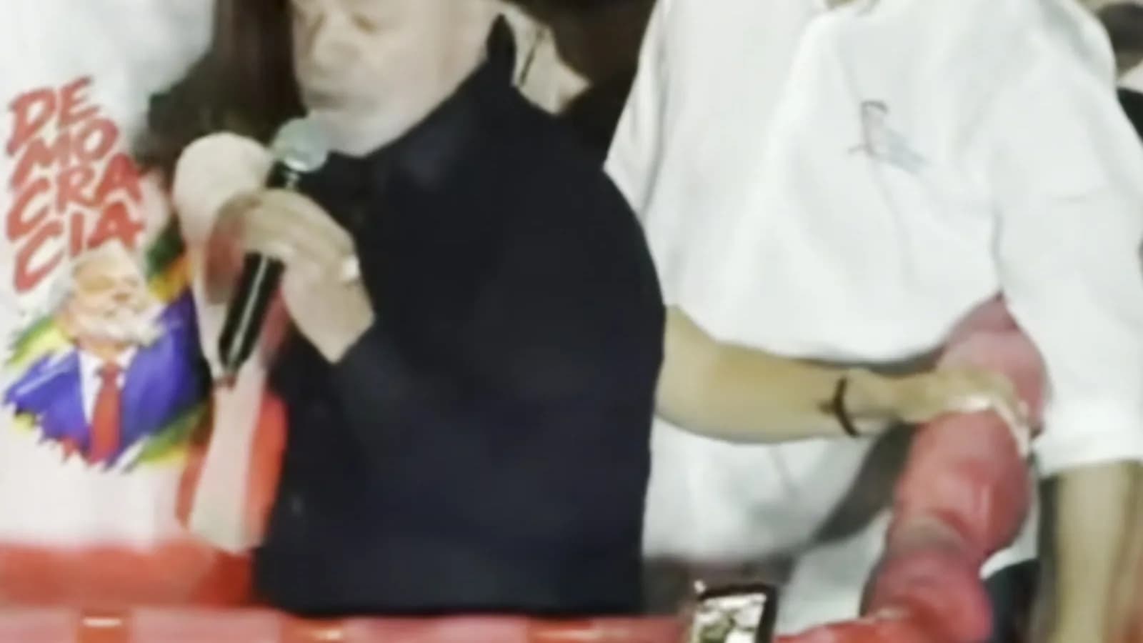 Lula discursa ao microfone de cima de carro de som, cercado por apoiadores durante ato de campanha à noite