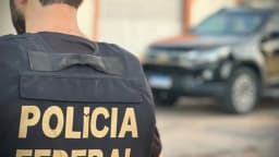 Agente da Polícia Federal de costas, com colete da corporação, em frente a uma viatura durante operação