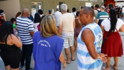 Eleitores em fila para votar, com integrante da Justiça Eleitoral do TRE-RJ ao fundo