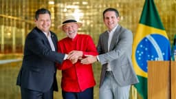 Davi Alcolumbre cumprimenta o presidente Lula de mãos dadas, com bandeira do Brasil ao fundo