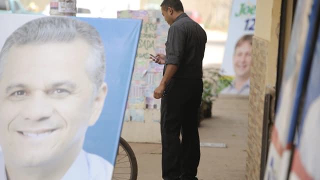 Homem observa material de propaganda eleitoral colado em poste na rua